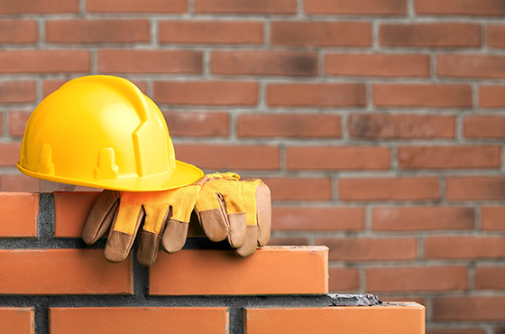 Symbolbild für Maurerarbeiten in Kellenhusen: Ziegelwand mit Bauhelm und Handschuhen.